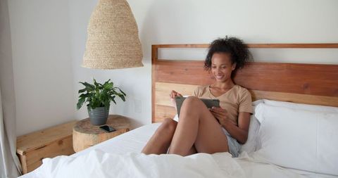Woman relaxing on bed using tablet in minimalist bedroom