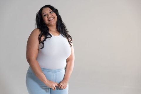 Confident plus-size woman smiling in white tank and denim jeans with neutral background