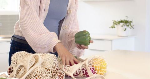 Woman organizing fresh produce in reusable mesh bags at home