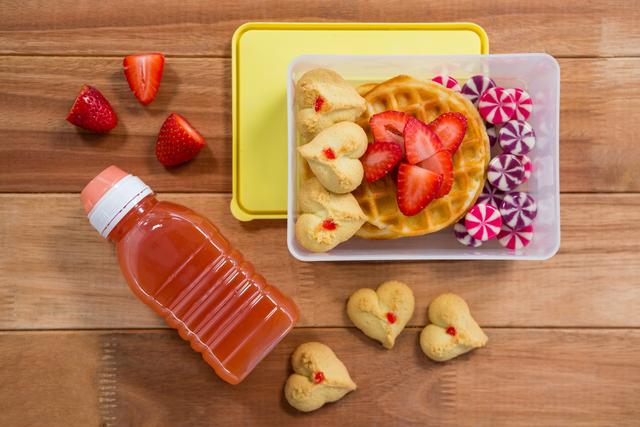 Sweet food and juice in lunch box on wooden table