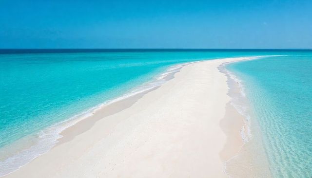 Aerial view showing stretching white sandbar tapering into turquoise ocean toward horizon