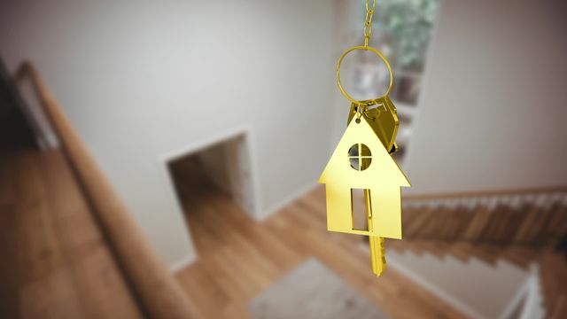 Video shows gold key attached to a house-shaped key ring, floating over a blurred home interior with wooden flooring and white walls. Ideal for use in real estate promotions, property sales advertisements, home buying services, moving companies, and residential investment marketing.