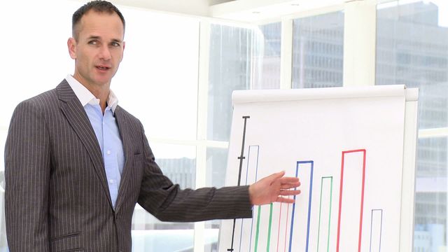 A businessman in a pinstripe suit presenting statistics on a bar chart in a bright office setting, ideal for conveying themes of business analysis, corporate strategy, leadership roles, and professional presentations. Useful for business blogs, corporate websites, and educational materials focusing on business intelligence and management practices.