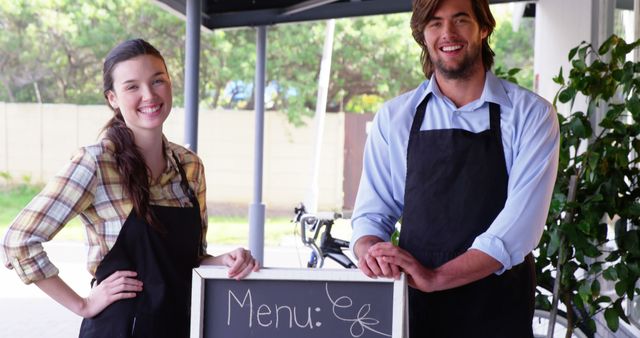 Smiling waiter and waitress standing with menu board outside the cafe 4k
