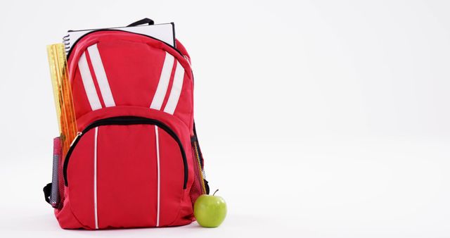 A red backpack with school supplies and a green apple indicates preparation for education. It symbolizes the importance of organization and nutrition in academic success.