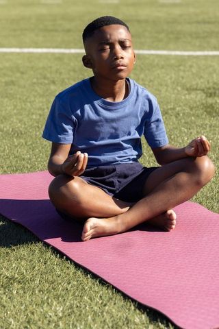 African american boy meditating cross-legged on yoga mat outdoors practicing mindfulness