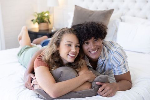 Relaxed multiracial couple cuddling on bed in bright bedroom, cozy romantic morning