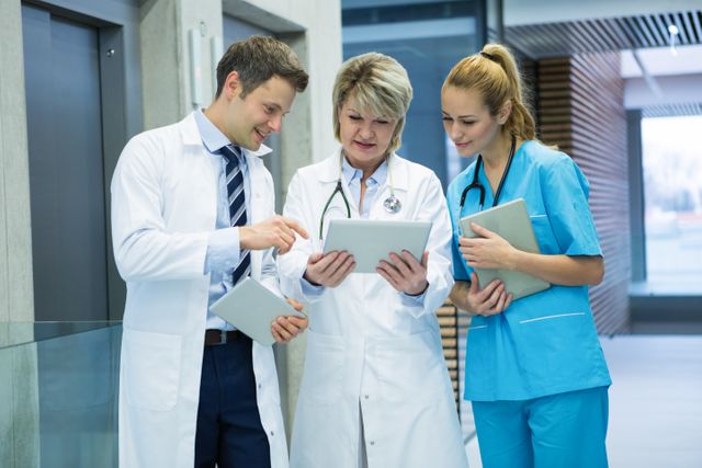 Medical professionals are collaborating in a hospital corridor, using a digital tablet to discuss patient data. This image is ideal for illustrating teamwork and technology in healthcare settings, medical consultations, and modern medical practices.