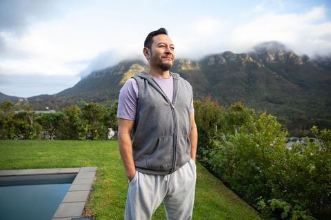Mature asian man standing by pool looking toward misty mountain horizon, serene morning