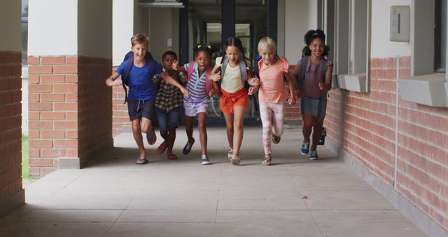 Diverse group of children running down outdoor school hallway, each child with a backpack. Ideal for educational content, back-to-school promotions, and children's clothing advertisements.