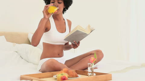 Woman Enjoys Breakfast in Bed While Reading a Book