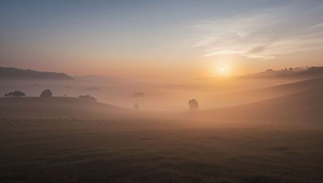 Glowing misty rolling hills at dawn with golden rising sun over pasture valleys