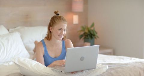 Woman Relaxing on Bed Using Laptop in Cozy Modern Bedroom