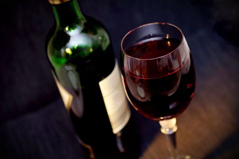 Rich Red Wine in Crystal Glass Featuring Blurred Bottle on Dark Elegant Backdrop