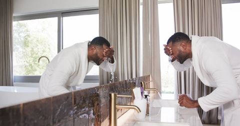 Man splashing face at double vanity in minimalist bathroom during morning routine