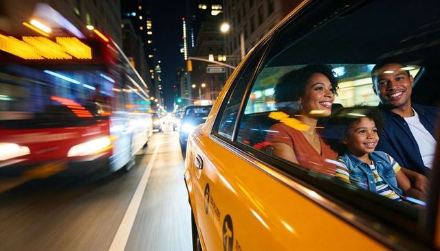 Smiling family enjoying nighttime taxi ride through busy city street with motion blur