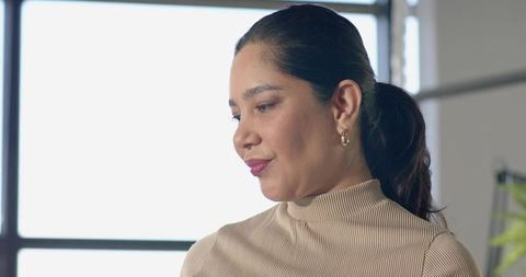 Professional mid-adult woman posing beside bright window grid in modern office headshot