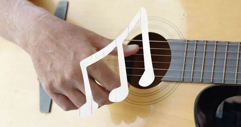 Plucking acoustic guitar strings close-up with hand over soundhole and musical note overlay