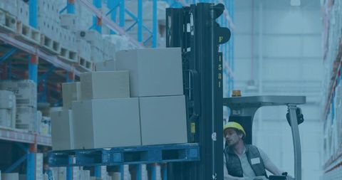 Forklift operator lifting loaded pallet in warehouse wearing hard hat and safety vest