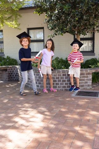 Multicultural kids celebrating graduation outdoors wearing caps and clutching diplomas