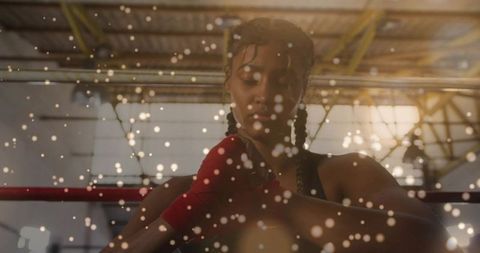 Female boxer tightening red hand wraps in industrial gym with dramatic bokeh lights