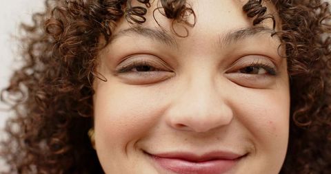 Smiling young woman with curly hair and freckles, natural studio headshot