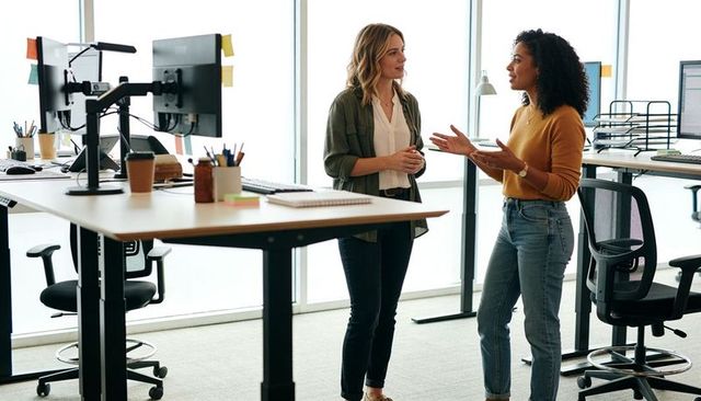 Two professional women collaborating at standing desks in bright modern office interior