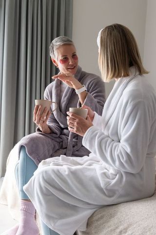 Two women having morning tea in robes with eye patches, cozy spa conversation