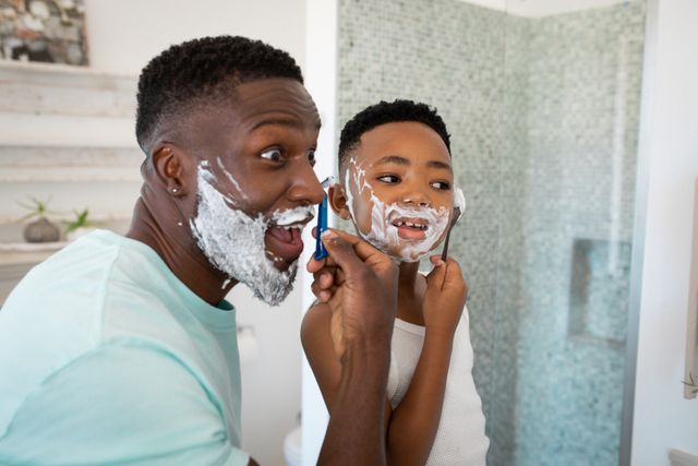 Father and son enjoying a playful moment while shaving together in the bathroom. Ideal for use in articles or advertisements about family bonding, parenting, morning routines, and personal grooming. Can also be used in campaigns promoting fatherhood, childhood memories, and home life.