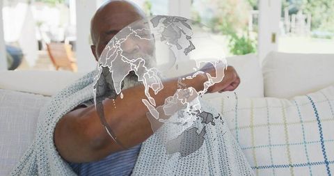 Senior african american man adjusting throw on couch with digital globe overlay