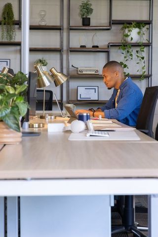 African american man working on laptop at modern coworking desk with plants and focus