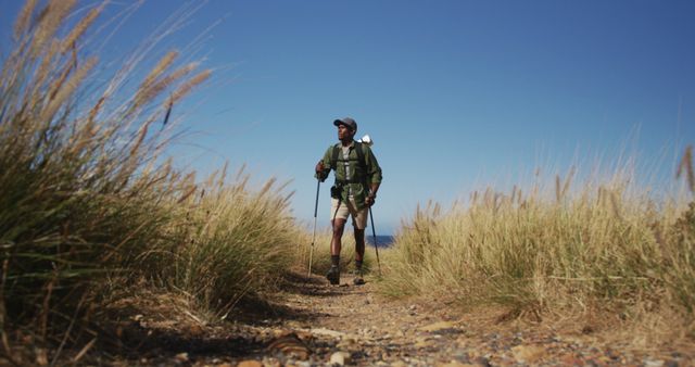African american man hiking with hiking poles in countryside by the coast. fitness training and healthy outdoor lifestyle.