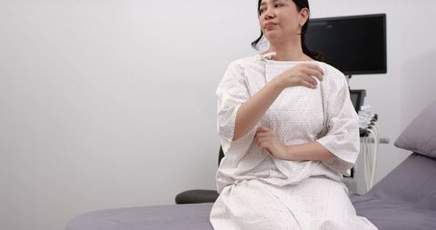 Woman preparing for ultrasound on exam bed wearing hospital gown and holding gown
