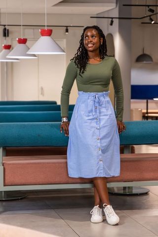 African american woman standing in modern coworking lounge in olive top and blue skirt