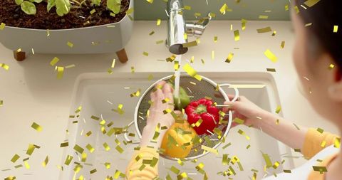 Washing colorful bell peppers under kitchen tap with gold confetti and indoor herb planter