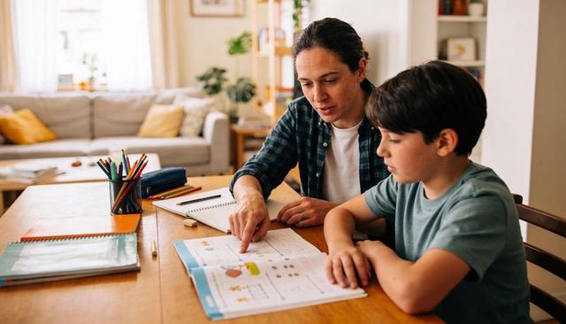 Parent tutoring child pointing at workbook guiding homework and learning at home