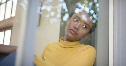 Contemplative Woman Reflecting by Sunlit Window Wearing Mustard Sweater