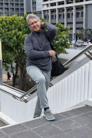 Senior man adjusting shoulder bag on city overpass stair landing, casual urban commuter