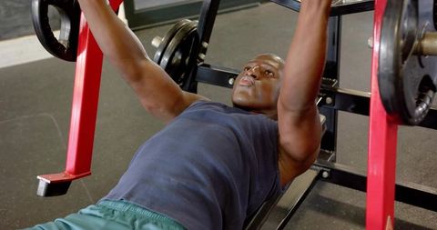 Focused man bench pressing loaded barbell on flat bench gym workout strength