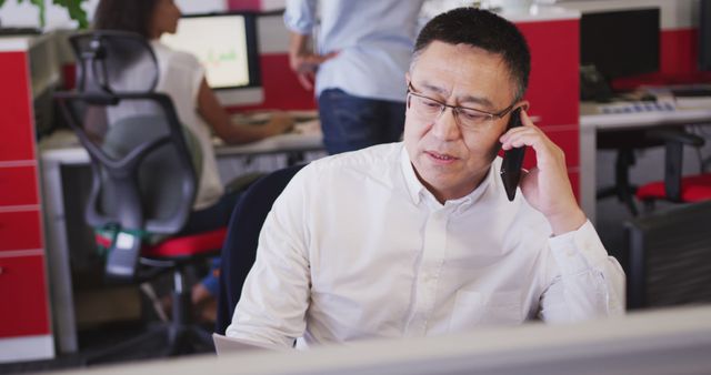 Asian businessman sitting at desk and talking on smartphone at office. Business, communication and work.