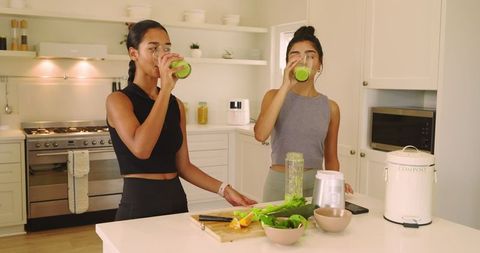 Two Friends Enjoying Fresh Green Smoothies in Modern Kitchen