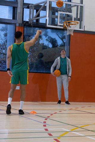 Male basketball teammates practicing shooting in indoor gym