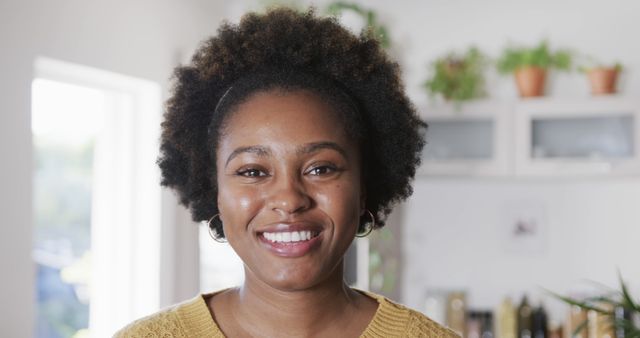 Young woman with natural afro hair smiling warmly. Suitable for lifestyle, positivity, and representation of natural beauty. Great for articles on self-confidence, joy, and modern home living.