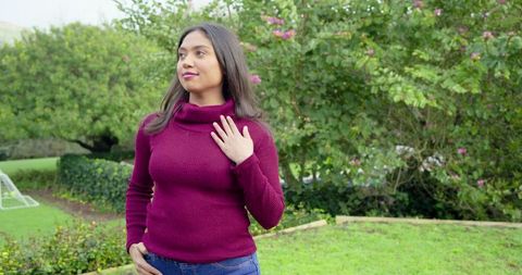 Young woman standing in backyard wearing maroon turtleneck sweater and jeans