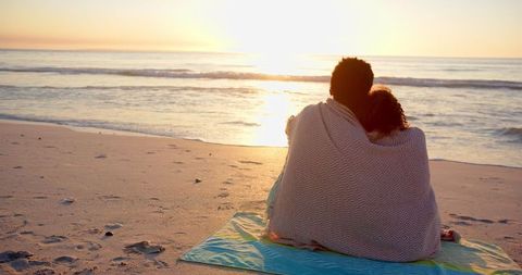 Biracial Couple Embraced in Blanket Admiring Sunset