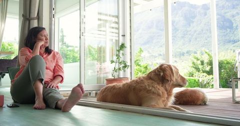 Mature woman relaxing by sliding doors with golden retrievers and mountain view