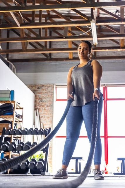 Asian woman working out with battle ropes in industrial gym for strength training