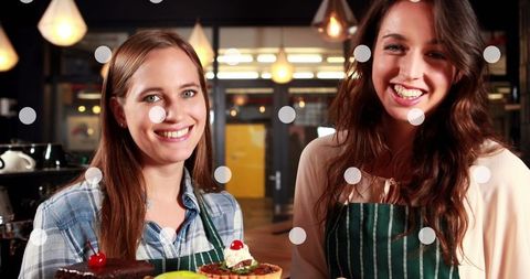 Smiling female bakers holding cakes in bakery shop