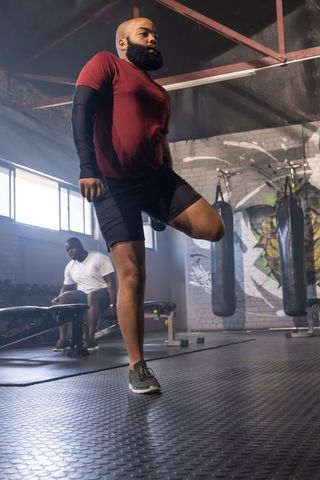 African american man performing single-leg balance exercise in urban gym with boxing bags