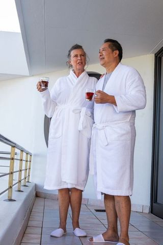 Senior couple relaxing on balcony in white bathrobes with tea